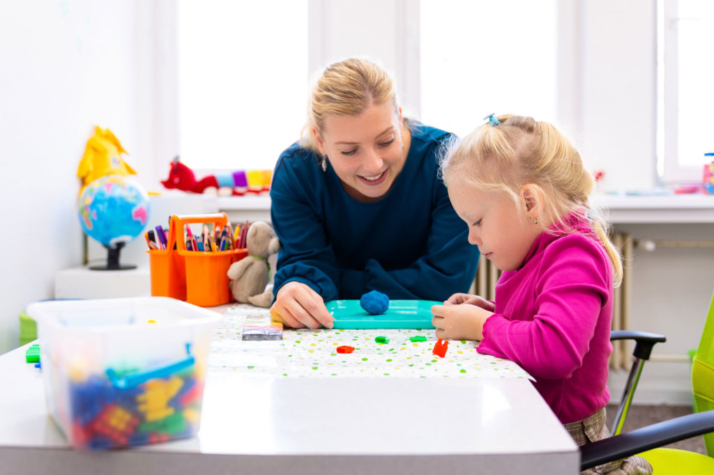 Toddler girl in child occupational therapy session doing sensory playful exercises with her therapist.